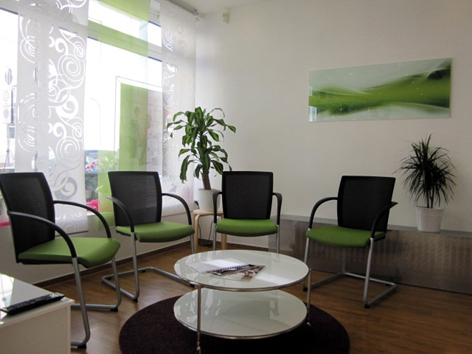 Heller Wartebereich mit modernen Stühlen, Pflanzen und rundem Tisch in einer Praxis.